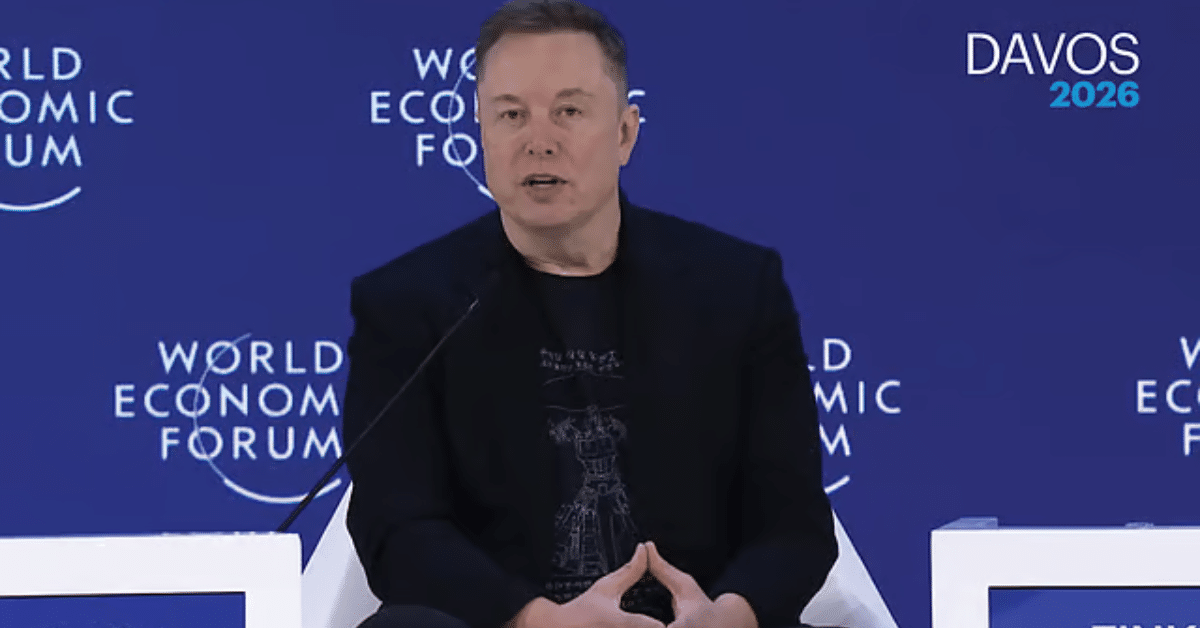 A technology executive speaking on stage at the World Economic Forum, seated against a blue backdrop labeled “World Economic Forum” and “Davos 2026,” addressing an audience during a panel discussion.
