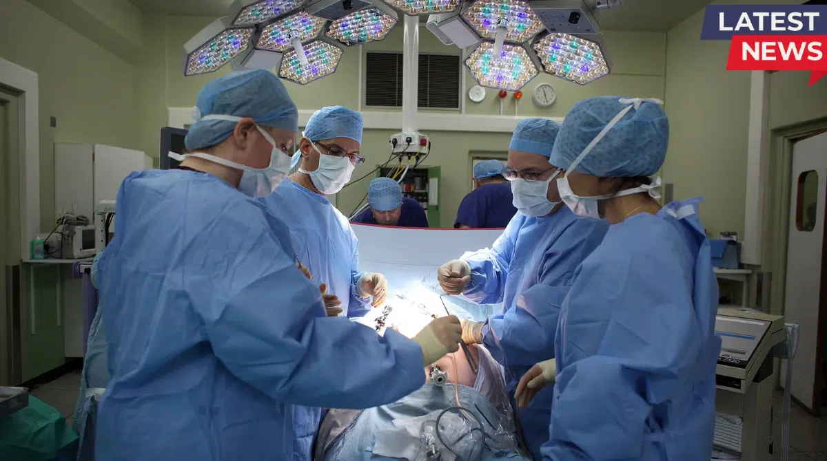 A team of surgeons wearing blue scrubs, masks, and caps performing a surgical procedure in a modern operating room under bright surgical lights.